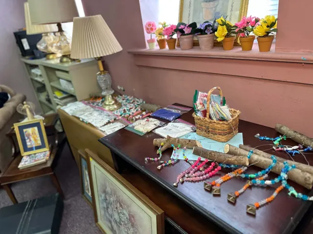 Colorful beaded jewelry, linens, lamps, and decorative flowers displayed in the thrift shop.