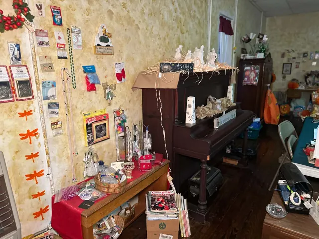 An upright piano and tables hold jewelry, craft supplies, books, and decorative items.