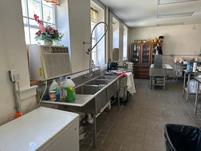 Stainless steel sinks and a tall spray faucet line the windows of the school kitchen.