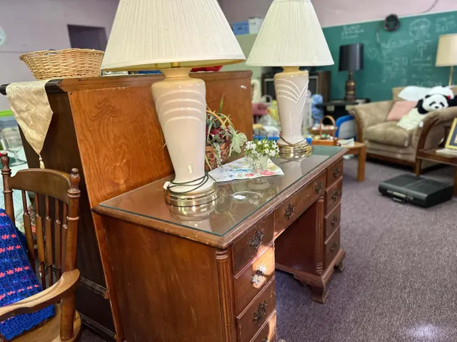 A wooden desk, two table lamps, a chair, and other furniture are arranged in a former classroom.
