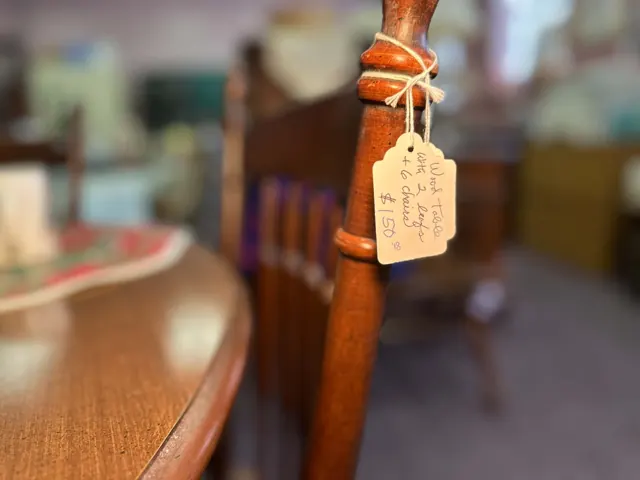 A handwritten price tag hangs from a wooden chair beside a dining table.