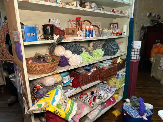 Shelves and baskets hold yarn, ribbon, glue, and small craft supplies.