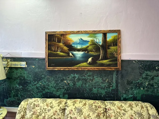 A framed landscape painting hangs above a floral sofa and an old classroom chalkboard.