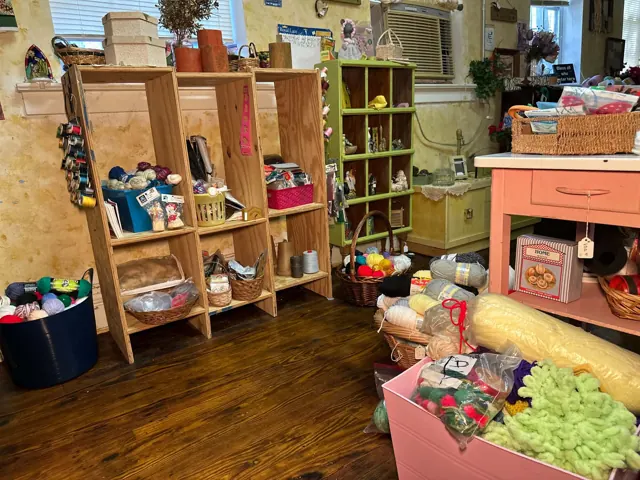 Open shelving, baskets, and a small table hold yarn and assorted craft supplies.
