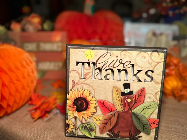 A Give Thanks turkey decoration stands in front of a display of orange pumpkins.