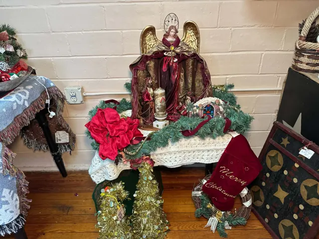 An angel figure, greenery, bows, a Christmas stocking, and other holiday decorations are displayed together.