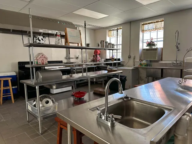 Stainless steel counters, sinks, shelving, ranges, and a large spray faucet inside the school kitchen.