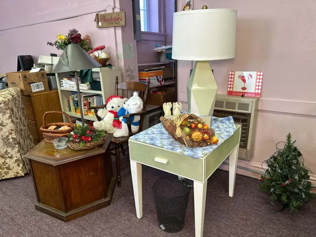 A table lamp, small tables, baskets, and decorative items are arranged in a former classroom.