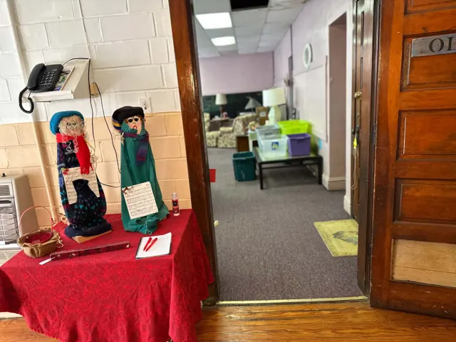 Seasonal decorations stand beside a wooden doorway leading into a room of thrift shop furniture.