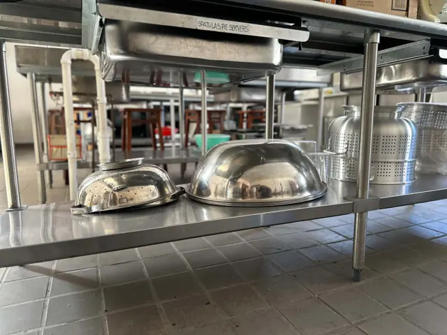 Metal colanders and other kitchen supplies sit on stainless steel shelving.