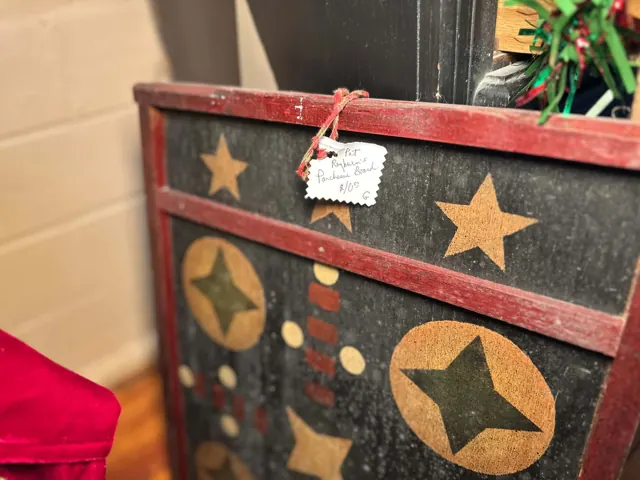 A wooden game board painted with stars has a handwritten tag identifying it as Pat Rayburn’s Parcheesi board.