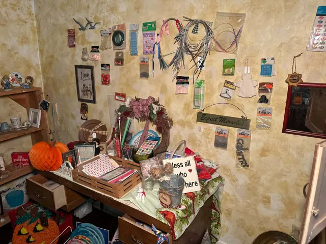 Craft supplies hang on a wall above a table filled with assorted decorative items and containers.