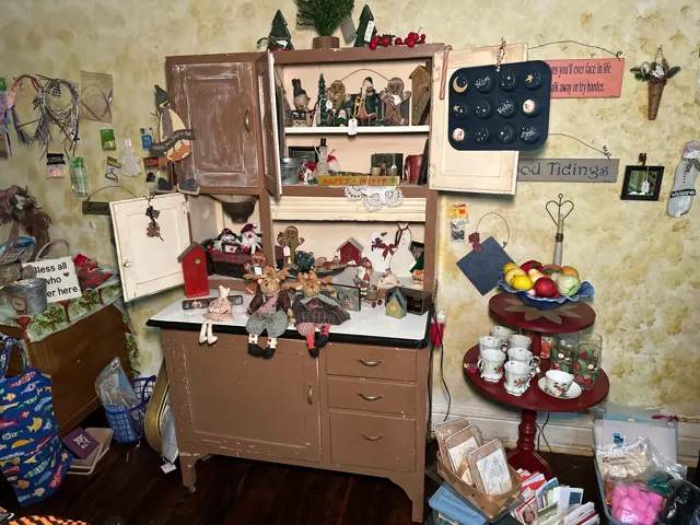 An open vintage cabinet holds holiday figures and decorations beside a small table of cups and saucers.