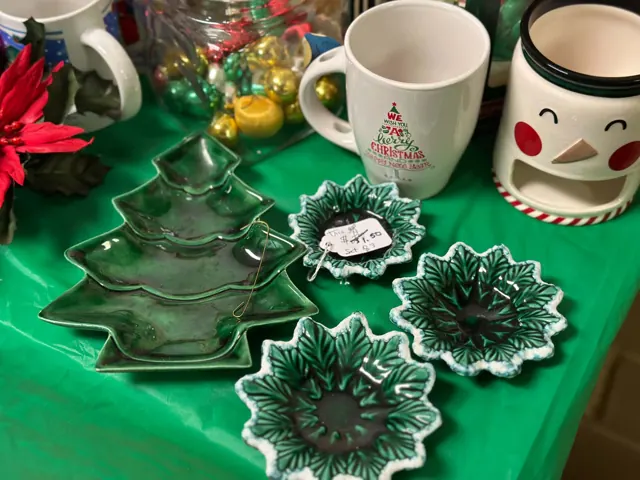 Green tree-shaped dishes, small bowls, Christmas mugs, and a snowman warmer are displayed on a green table.