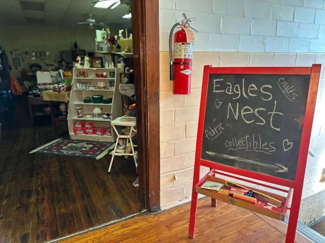 A red chalkboard sign listing crafts, fabric, and collectibles stands beside the open Eagles Nest doorway.