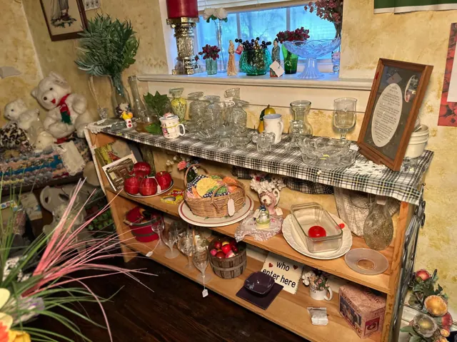 Glass vases, bowls, cups, plates, baskets, and other housewares fill a thrift shop shelf.
