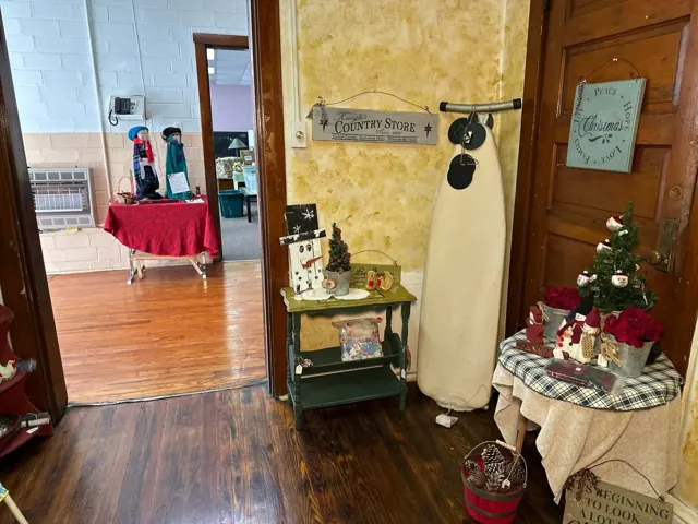 An upright ironing board stands beside a small shelf, seasonal signs, and a table of Christmas decorations.
