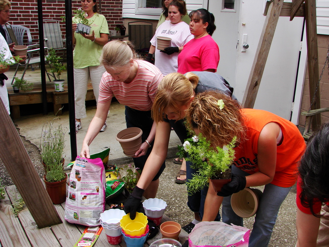A group working with potted plants outdoors beside the brick building.