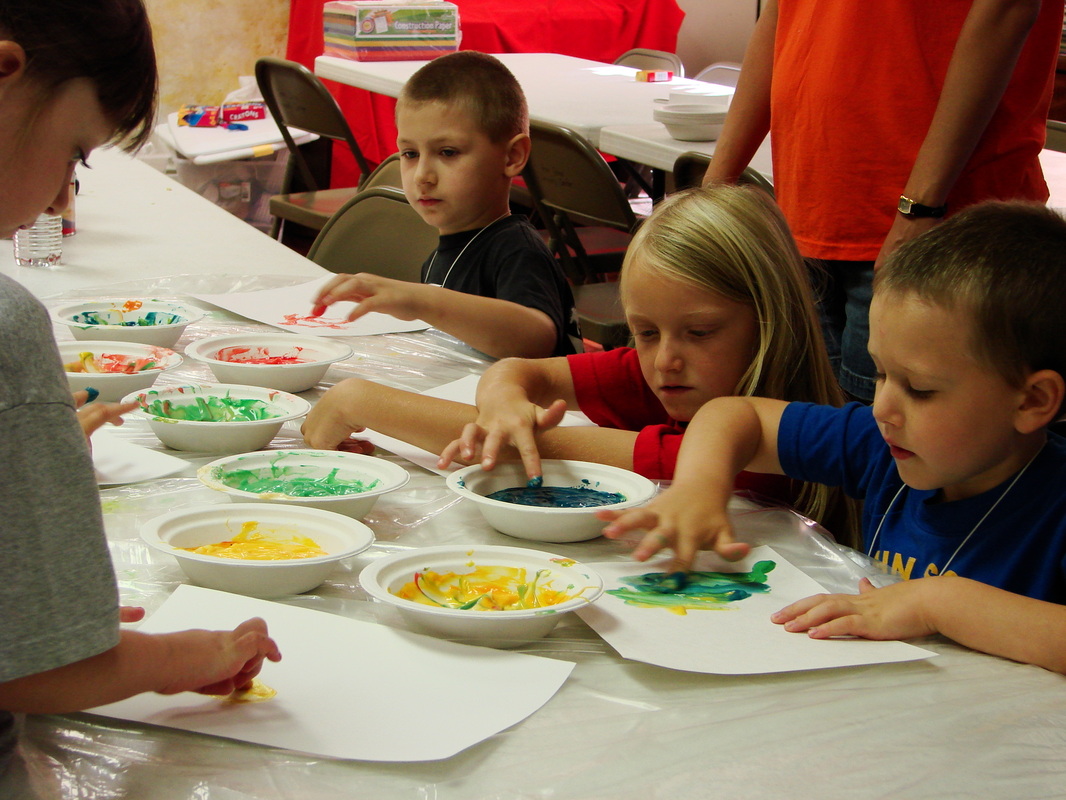 Children working with plates of paint at a table.