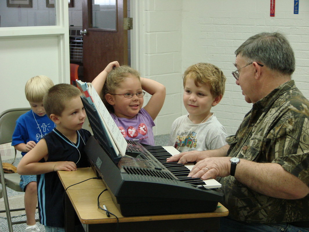 Children gathered beside an adult at an electronic keyboard.