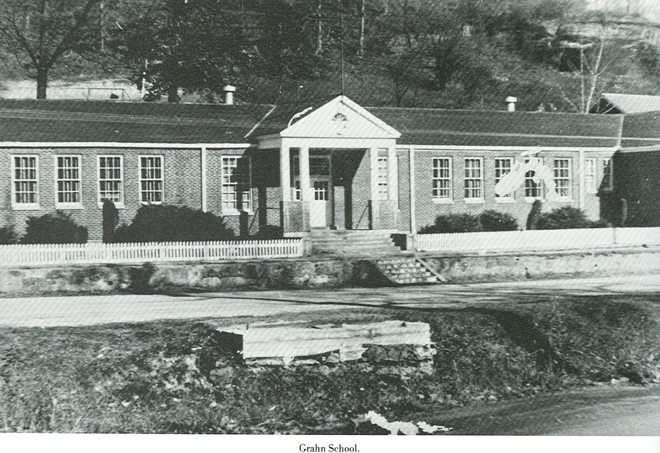 Historic photograph of Grahn School, with white entrance columns, classroom windows, a picket fence and a stone-lined approach.